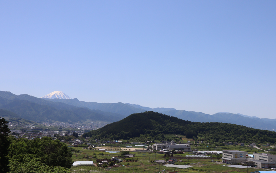 富士山と手前にはいくつかの山々、街並みが広がっている画像