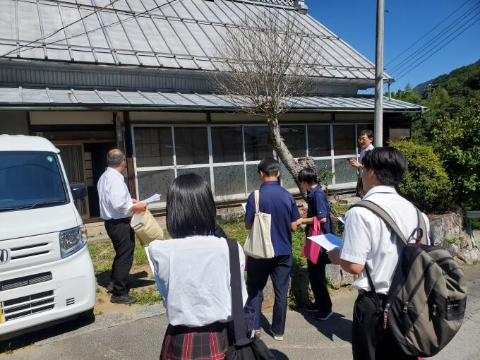 空き家について屋外で説明する市職員とそれを聞く高校生たちの画像